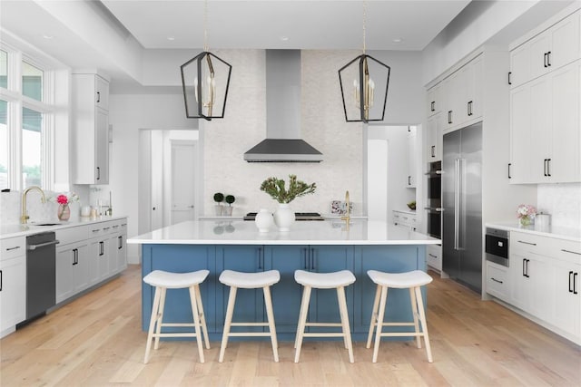 kitchen with light countertops, wall chimney range hood, and decorative light fixtures