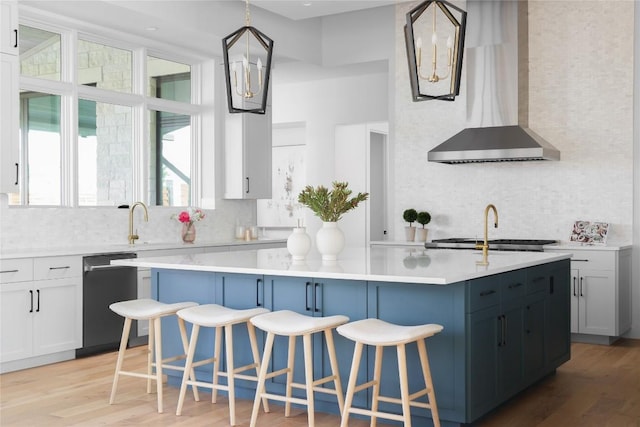 kitchen featuring black dishwasher, decorative light fixtures, light countertops, a kitchen island, and wall chimney range hood