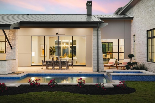 back of property at dusk featuring a ceiling fan, metal roof, a standing seam roof, a patio area, and a pool with connected hot tub