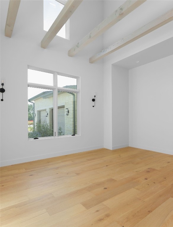 spare room with light wood-type flooring, a towering ceiling, and baseboards