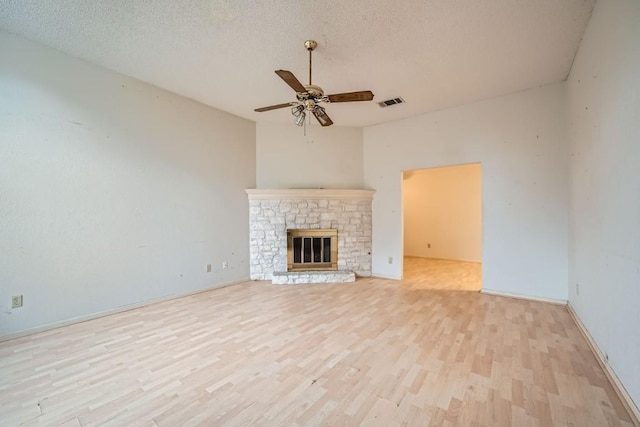 unfurnished living room featuring ceiling fan, a fireplace, a textured ceiling, and light wood-type flooring