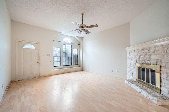 unfurnished living room featuring a textured ceiling, vaulted ceiling, ceiling fan, a fireplace, and light hardwood / wood-style floors