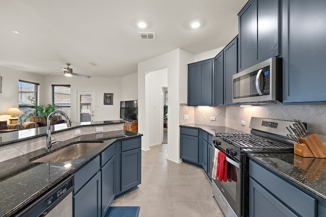 kitchen with dark stone counters, blue cabinets, sink, ceiling fan, and stainless steel appliances