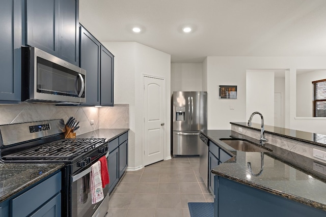 kitchen with appliances with stainless steel finishes, dark stone counters, blue cabinets, sink, and light tile patterned floors