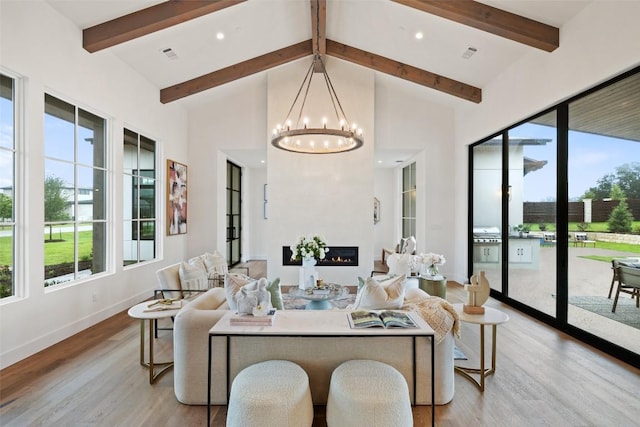 living area featuring light wood finished floors, a glass covered fireplace, beam ceiling, and an inviting chandelier