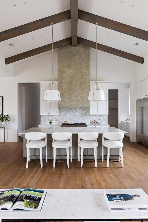 kitchen with white cabinetry, hanging light fixtures, tasteful backsplash, high vaulted ceiling, and a breakfast bar area