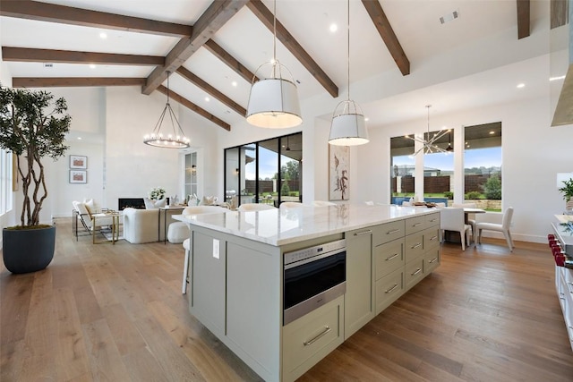 kitchen featuring beam ceiling, decorative light fixtures, a kitchen island, and light hardwood / wood-style flooring