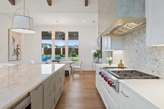 kitchen with wall chimney range hood, white cabinetry, light stone counters, and decorative light fixtures