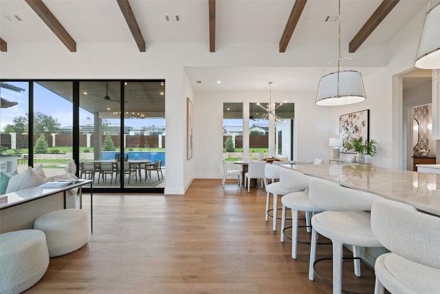 interior space with beam ceiling, light stone counters, hanging light fixtures, and hardwood / wood-style floors