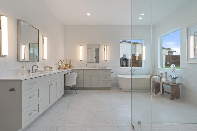 bathroom featuring recessed lighting, two vanities, a sink, marble finish floor, and a soaking tub