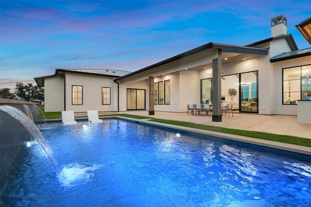 back house at dusk featuring pool water feature and a patio