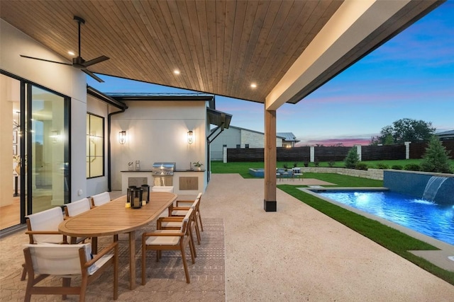 patio terrace at dusk with an outdoor pool, an outdoor kitchen, a ceiling fan, fence, and outdoor dining area