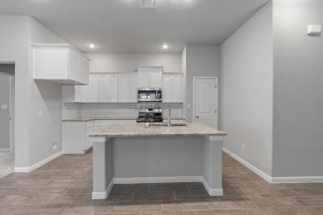 kitchen with sink, light stone counters, an island with sink, white cabinets, and appliances with stainless steel finishes