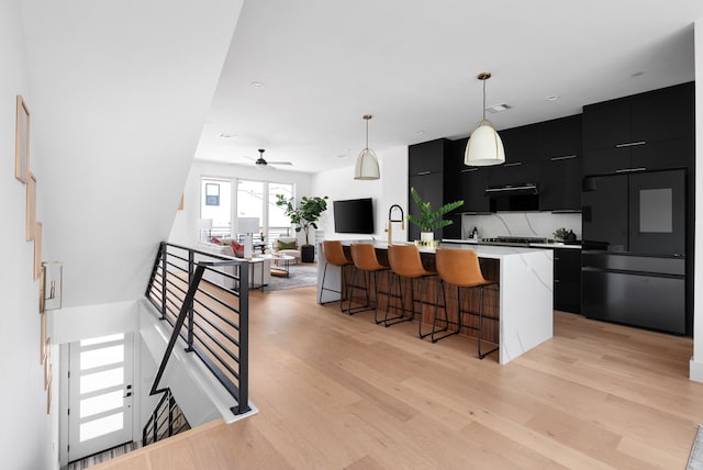 kitchen with decorative light fixtures, paneled built in refrigerator, a kitchen island with sink, and light hardwood / wood-style flooring