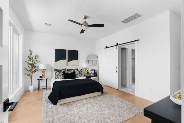 bedroom featuring wood-type flooring, ceiling fan, and a barn door