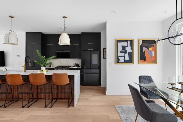 kitchen featuring pendant lighting, light hardwood / wood-style flooring, paneled built in fridge, a kitchen breakfast bar, and a center island with sink