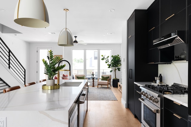 kitchen with pendant lighting, sink, light stone countertops, a center island with sink, and stainless steel appliances