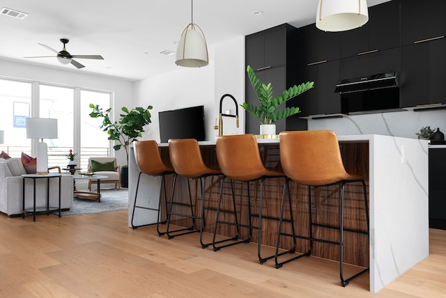 kitchen featuring decorative light fixtures, light wood-type flooring, a kitchen breakfast bar, and ceiling fan