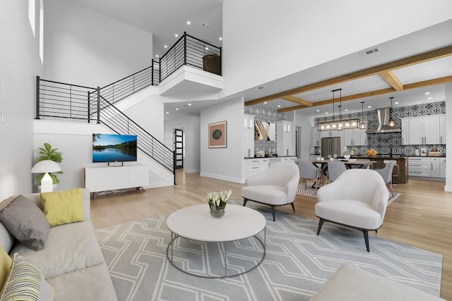 living room with beamed ceiling, coffered ceiling, a high ceiling, and light wood-type flooring