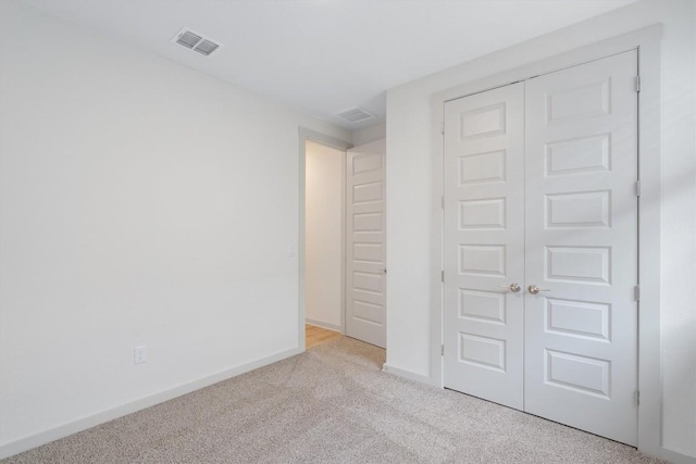 unfurnished bedroom featuring visible vents, baseboards, light colored carpet, and a closet