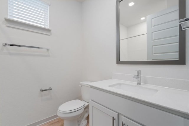 bathroom featuring toilet, wood finished floors, baseboards, vanity, and recessed lighting
