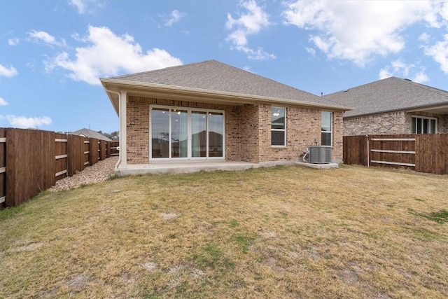 rear view of property featuring cooling unit, a fenced backyard, brick siding, and a lawn