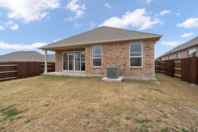 rear view of property with cooling unit, roof with shingles, a yard, a fenced backyard, and brick siding