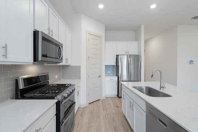 kitchen with a sink, appliances with stainless steel finishes, white cabinets, and light wood finished floors