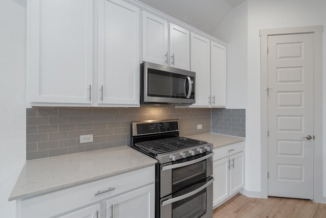 kitchen with light stone countertops, light wood-style flooring, stainless steel appliances, white cabinets, and tasteful backsplash