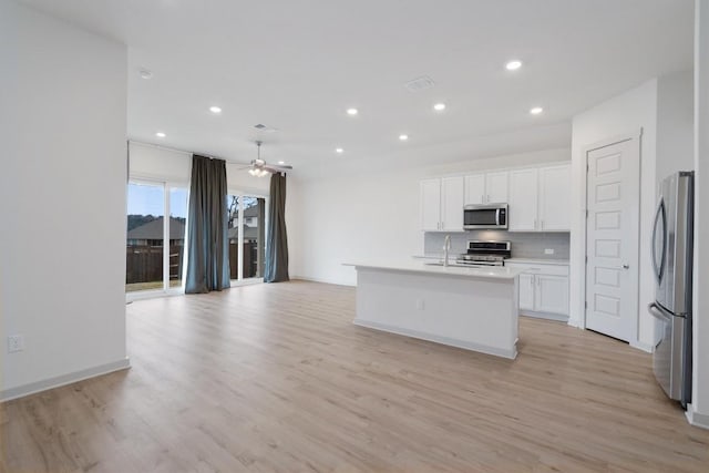 kitchen with light wood-type flooring, decorative backsplash, stainless steel appliances, white cabinetry, and a kitchen island with sink