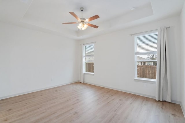 unfurnished room with a tray ceiling, light wood-style floors, baseboards, and ceiling fan