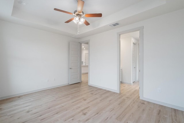 empty room with visible vents, baseboards, ceiling fan, light wood-style flooring, and a raised ceiling