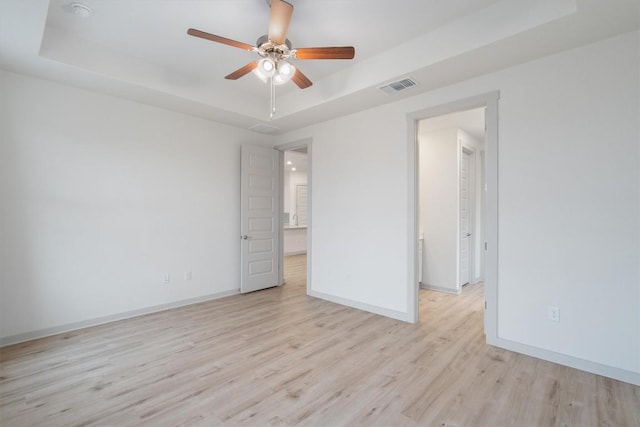 unfurnished room with a ceiling fan, baseboards, visible vents, a raised ceiling, and light wood-type flooring
