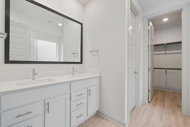 full bath with double vanity, a spacious closet, wood finished floors, and a sink