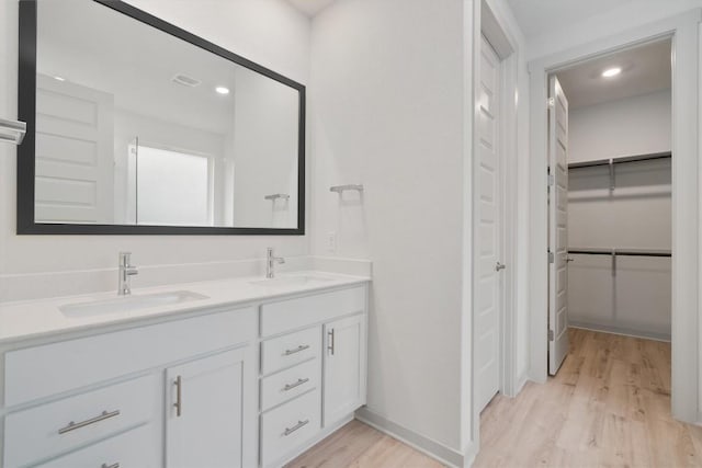 full bathroom featuring double vanity, wood finished floors, a walk in closet, and a sink