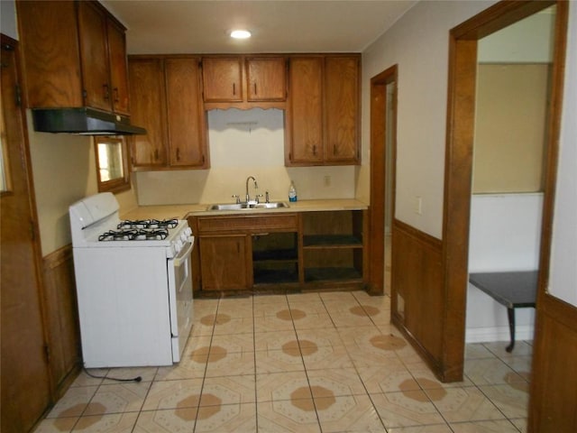 kitchen featuring white gas range, wood walls, sink, and light tile patterned floors