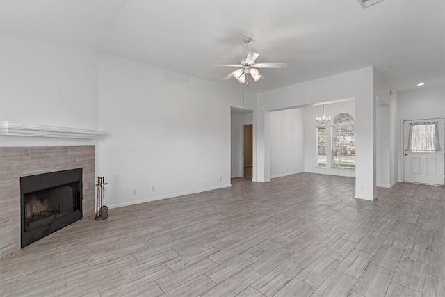 unfurnished living room with ceiling fan with notable chandelier and a tiled fireplace