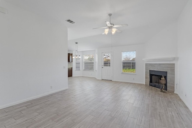 unfurnished living room featuring ceiling fan with notable chandelier, vaulted ceiling, and a tiled fireplace