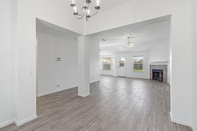 unfurnished living room featuring ceiling fan with notable chandelier and a tiled fireplace