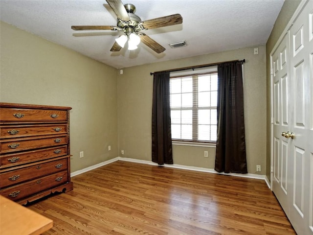 unfurnished bedroom with a textured ceiling, a closet, light hardwood / wood-style flooring, and ceiling fan