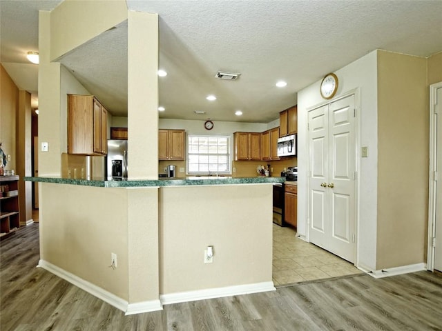 kitchen with stainless steel appliances, a textured ceiling, and light hardwood / wood-style floors