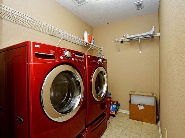 clothes washing area with separate washer and dryer, a textured ceiling, and light tile patterned floors