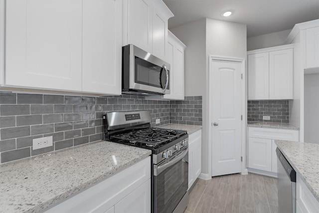 kitchen with white cabinets, appliances with stainless steel finishes, tasteful backsplash, and light stone counters