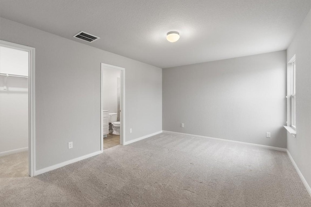 unfurnished bedroom with light carpet, a walk in closet, ensuite bathroom, multiple windows, and a closet