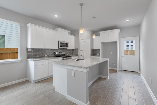 kitchen with a kitchen island with sink, white cabinets, stainless steel appliances, and decorative light fixtures