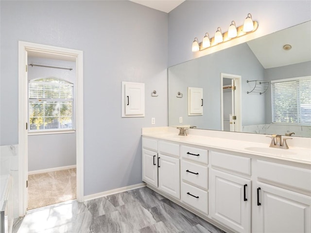 full bathroom featuring a sink, baseboards, double vanity, and vaulted ceiling