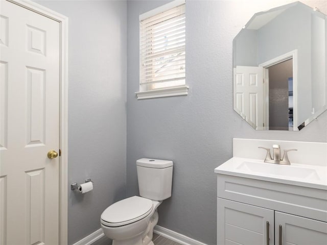 half bath with baseboards, toilet, and vanity