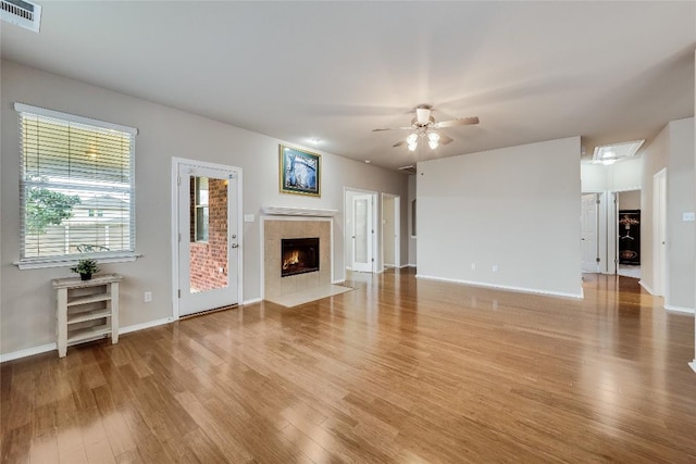 unfurnished living room featuring a tiled fireplace, ceiling fan, and light hardwood / wood-style flooring