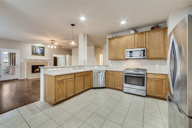 kitchen featuring ceiling fan, stainless steel appliances, pendant lighting, a tiled fireplace, and decorative backsplash