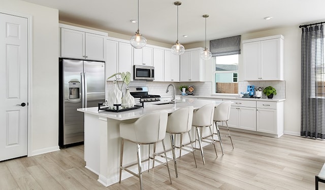 kitchen featuring pendant lighting, sink, a kitchen island with sink, appliances with stainless steel finishes, and white cabinets